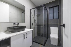 Ein modernes Badezimmer mit einer gläsernen Dusche, einem weißen Waschbecken mit großem Becken und einer Toilette.