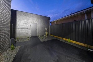 Ein gepflasterter Weg führt zu einem Gebäude mit Ziegelverkleidung und einem Metallzaun.