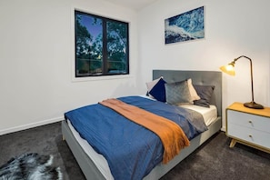 A bedroom with a bed, a nightstand, a lamp, a rug, and a dog.