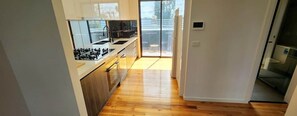 A modern kitchen with a central island, a dining area with a table and chairs, and a sliding glass door leading to an outdoor space. - Modern Luxury Living House (Fawkner)