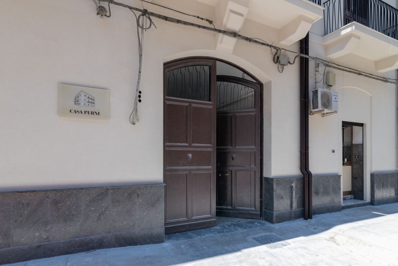 A building entrance with a large wooden door, a sign reading 'CASA PERNI,' and an air conditioning unit on the wall.