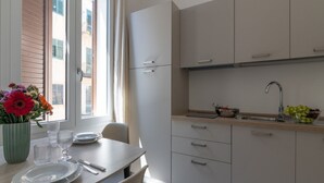 Uma cozinha moderna com armários brancos, uma mesa de jantar posta com pratos e copos, e uma janela com vista para edifícios.