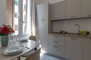 Eine moderne Küche mit weißen Schränken, einem Tisch gedeckt mit Tellern und Gläsern, und einem Fenster mit Blick auf Gebäude.