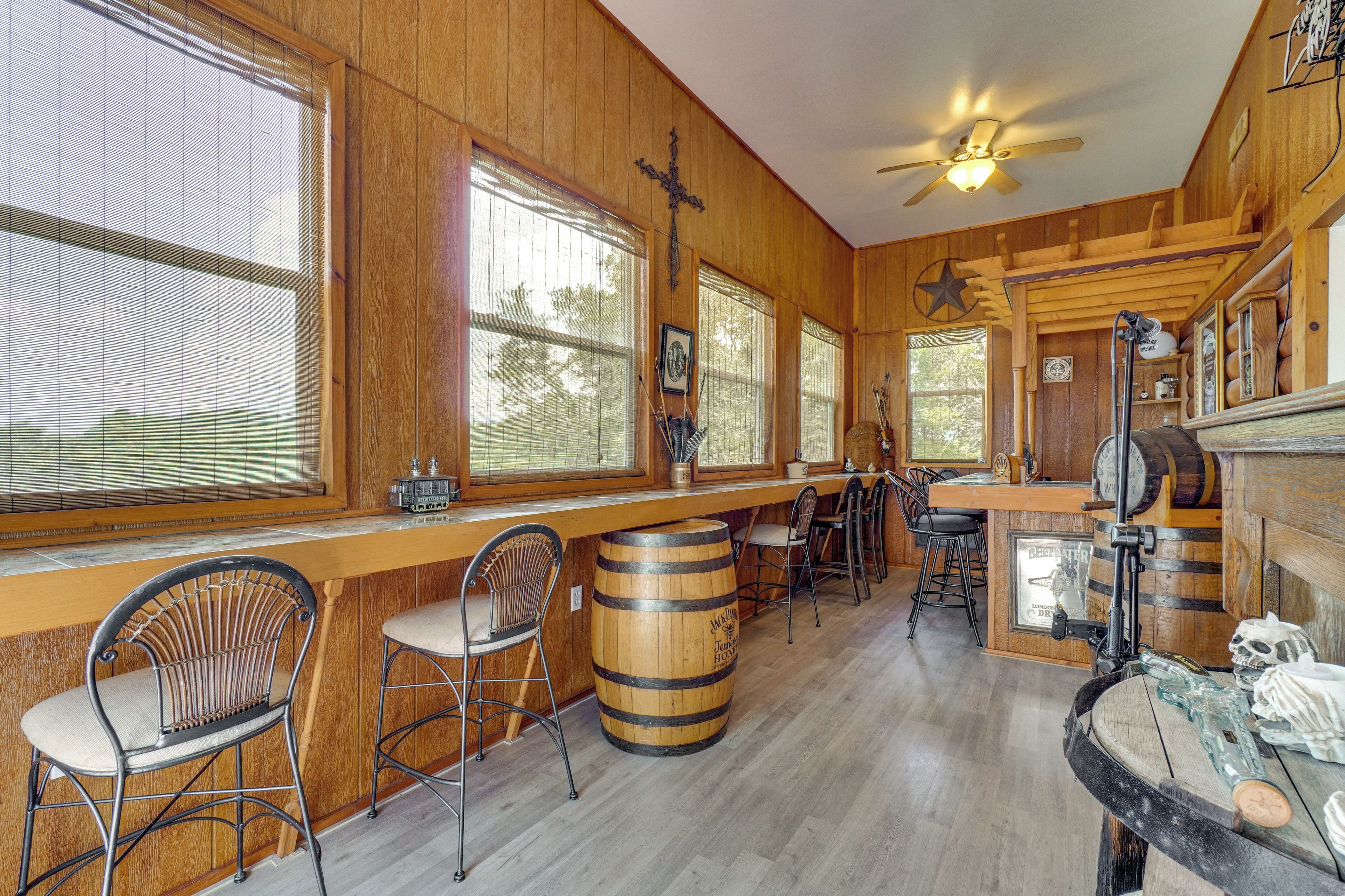 A rustic bar area with wooden walls, large windows, and a ceiling fan.