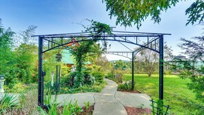Un vialetto in giardino che conduce a un arco in metallo, con una panchina e un lampione.