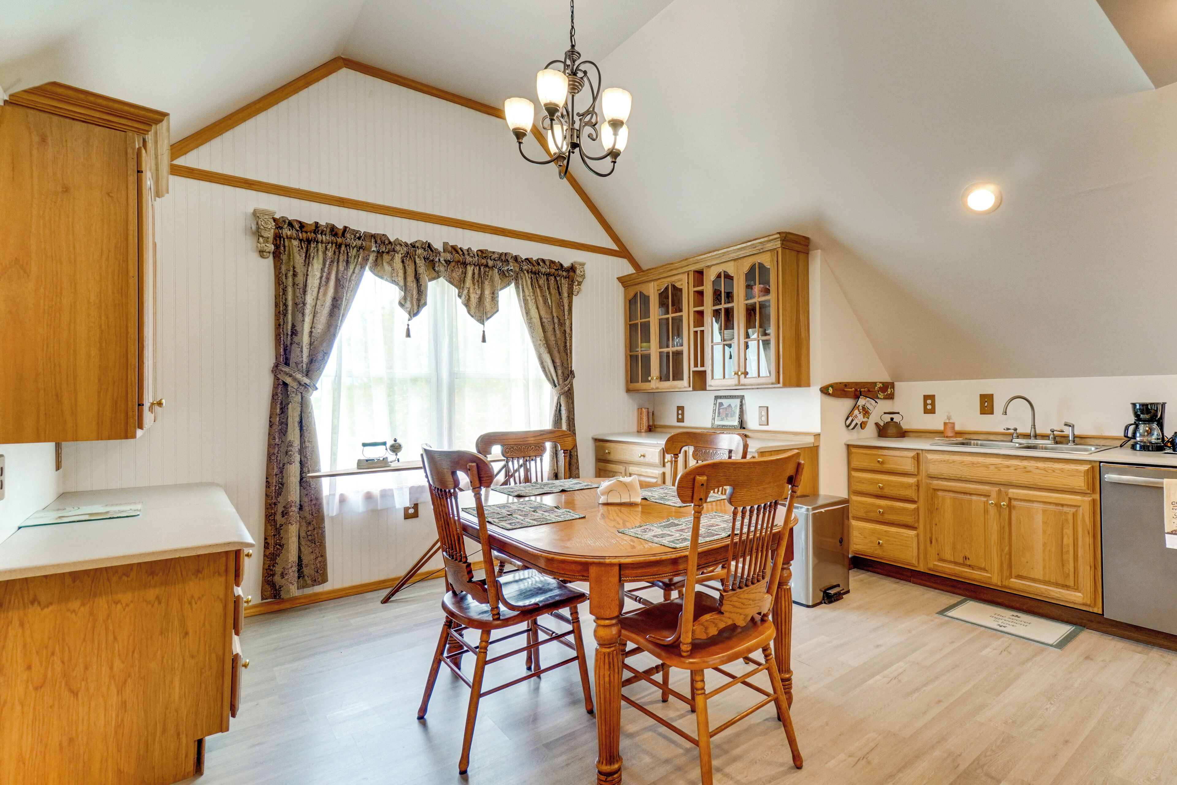 A dining area with a wooden table and chairs, a chandelier, and a kitchen with wooden cabinets and a sink.