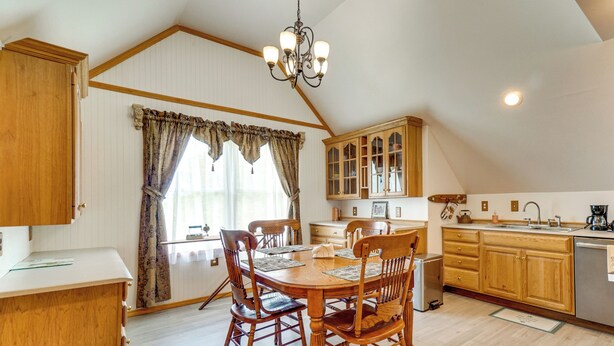 Un'area pranzo con tavolo e sedie in legno, un lampadario e una cucina con mobili in legno e un lavello.