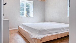 A bedroom with a wooden bed, a window with a view of trees, and a white wall. - Cozy home in Højer with WiFi (Højer)