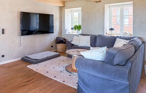 A living room with a grey sofa, a flat-screen TV mounted on the wall, a round coffee table, and a wooden floor. - Cozy home in Højer with WiFi (Højer)