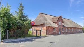 A traditional brick building with a thatched roof, a red circular sign with a crest, and a clear sky. - Cozy home in Højer with WiFi (Højer)