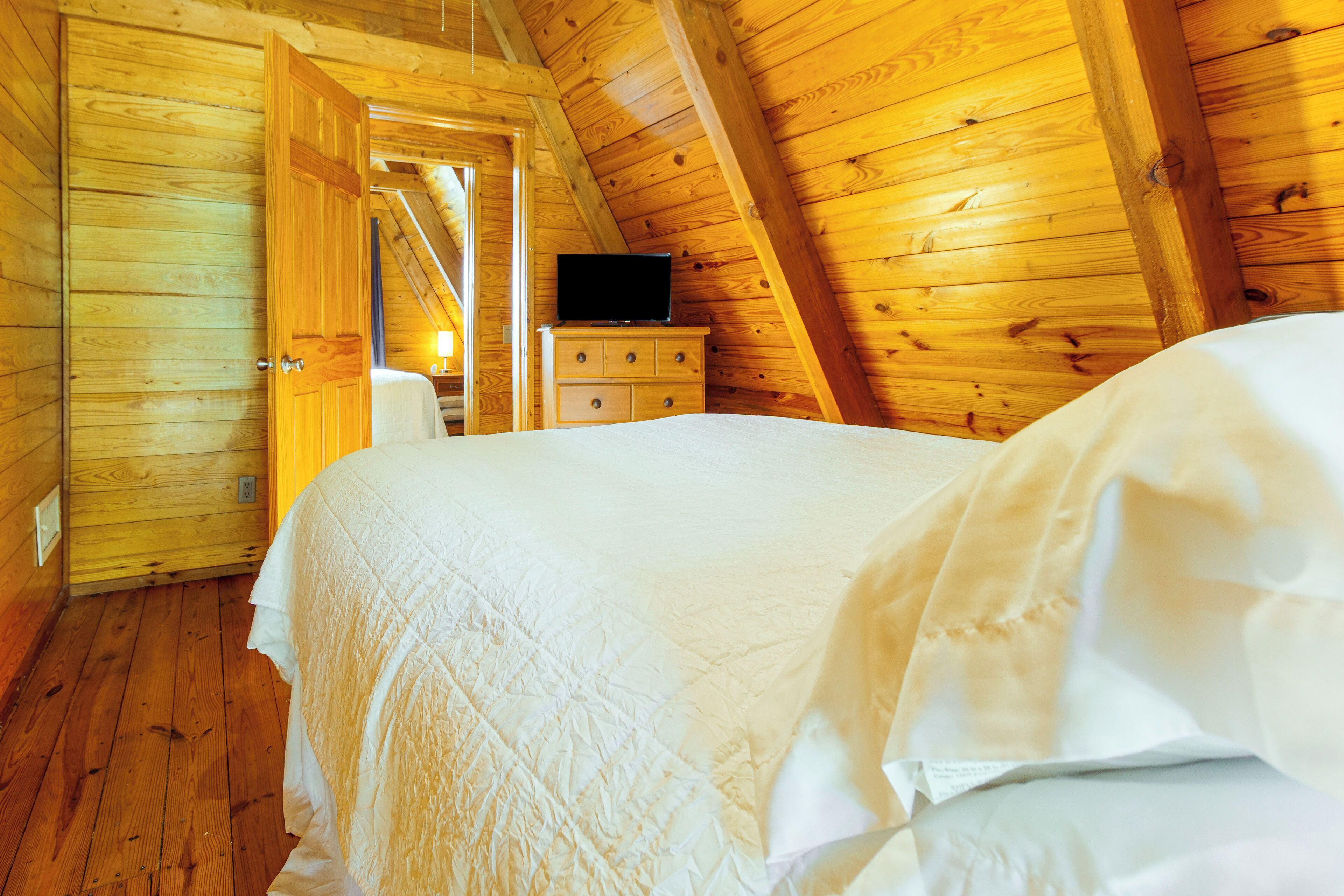 Ein Zimmer aus Holz mit einem Bett, einer Kommode und einem Fernseher auf der Kommode.