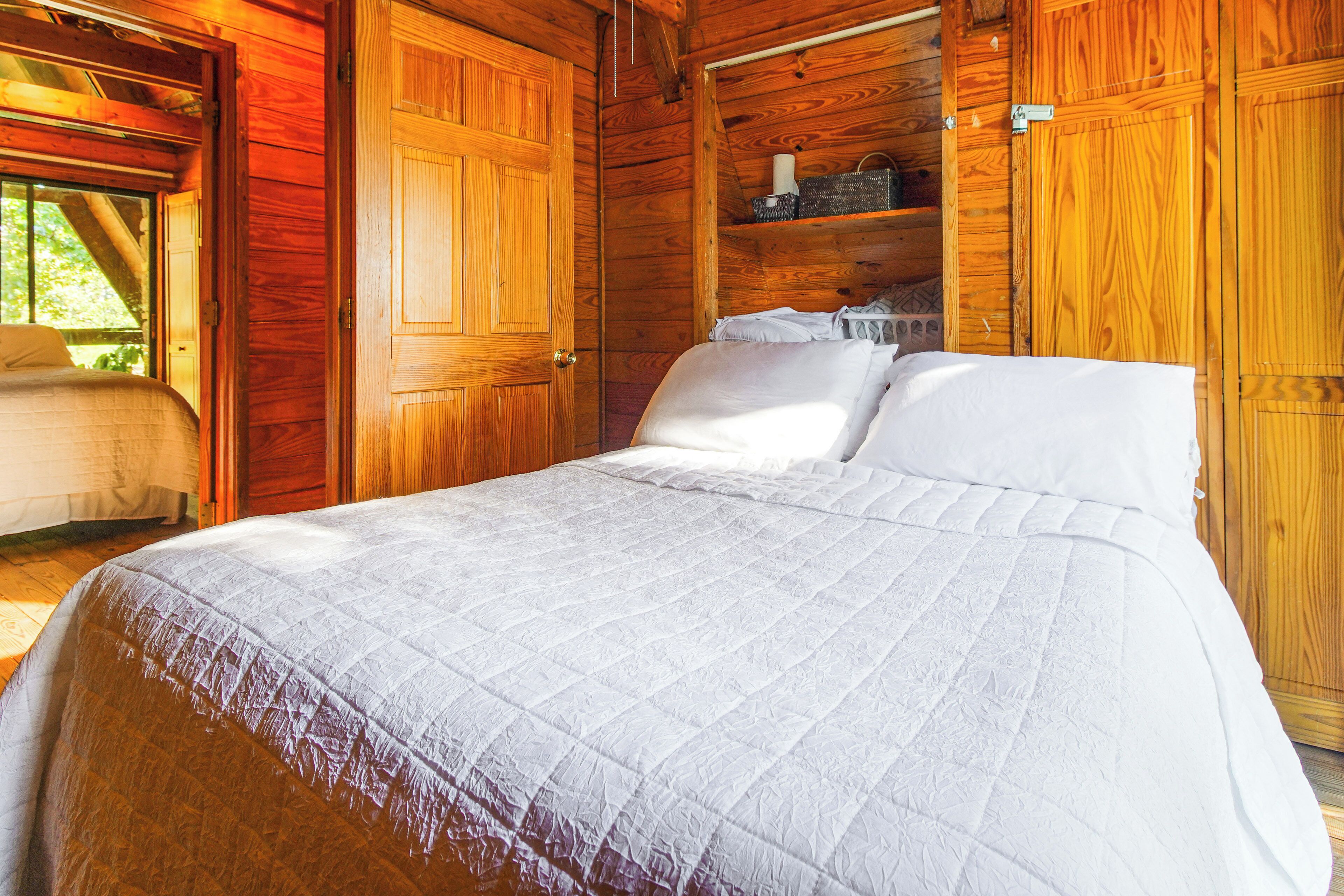 A wooden cabin bedroom with a bed, a shelf with items, and a door leading outside.