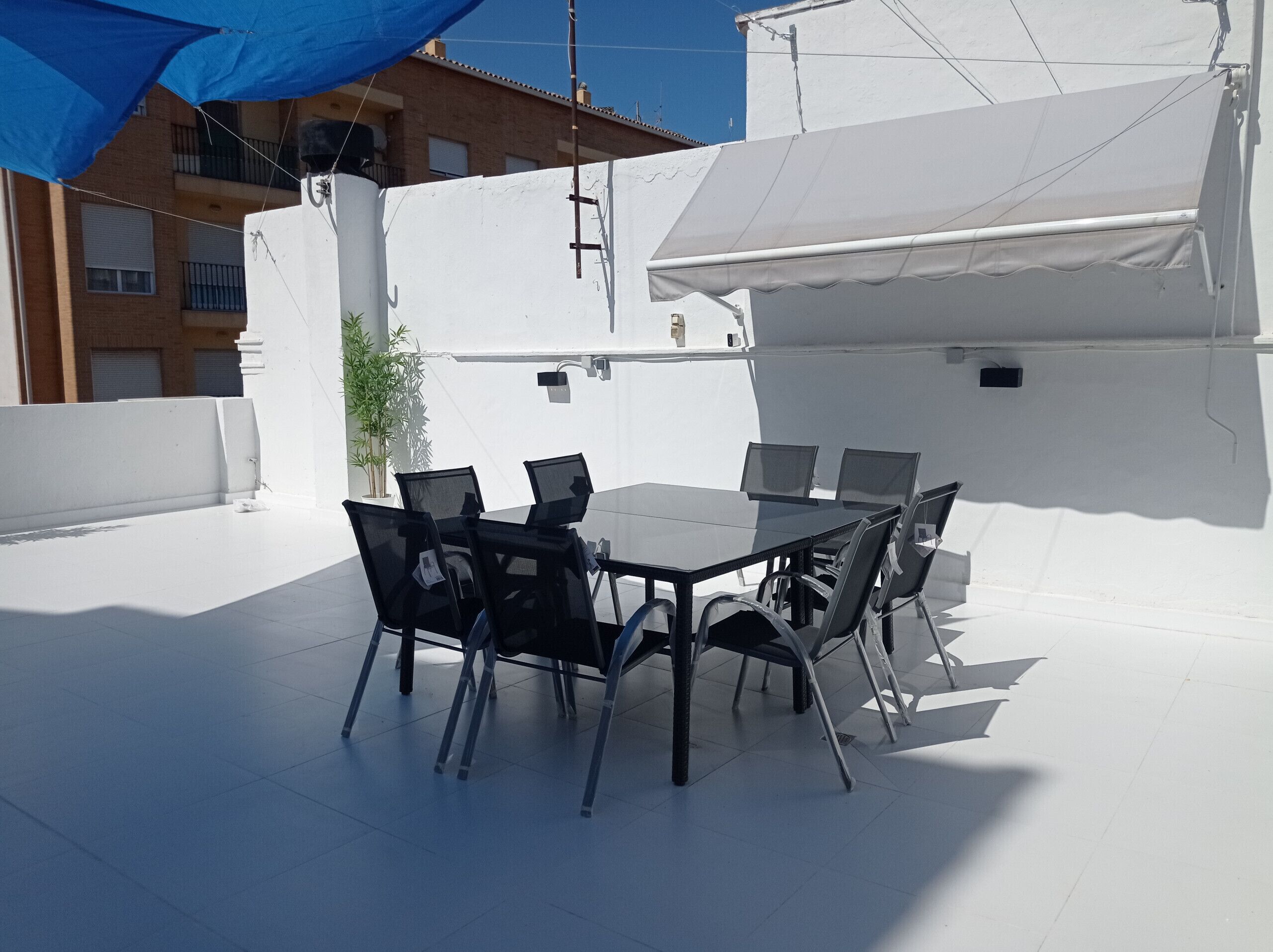Eine Terrasse im Freien mit Tisch und Stühlen, einem weißen Zelt und einem Gebäude im Hintergrund.