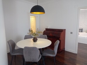 Ein Essbereich mit einem runden Tisch, sechs Stühlen, einer Blumenvase, einer schwarzen Pendelleuchte und einem Kamin.