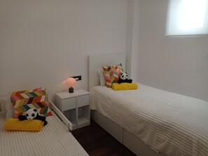Un dormitori amb dos llits, una taula de nit amb una làmpada i coixins decoratius.