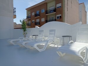 Eine Dachterrasse mit weißen Liegestühlen und einem kleinen Tisch, umgeben von einer weißen Mauer.