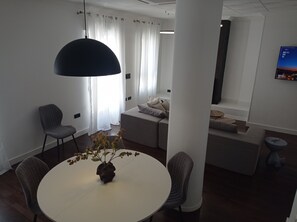 Ein modernes Wohnzimmer mit einem runden weißen Tisch, grauen Stühlen, einer Couch und einer großen schwarzen Pendelleuchte.