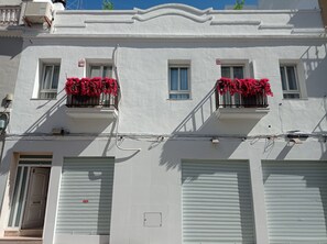 Edifici amb parets exteriors blanques, nombroses finestres i balcons amb flors vermelles.