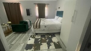 A bedroom with a bed, a green armchair, a small table with a vase, and a patterned rug.