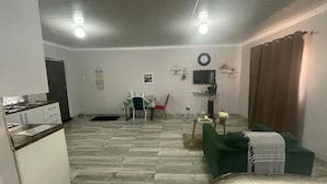 A compact living space with a kitchenette, a dining area, a green sofa, and a television.
