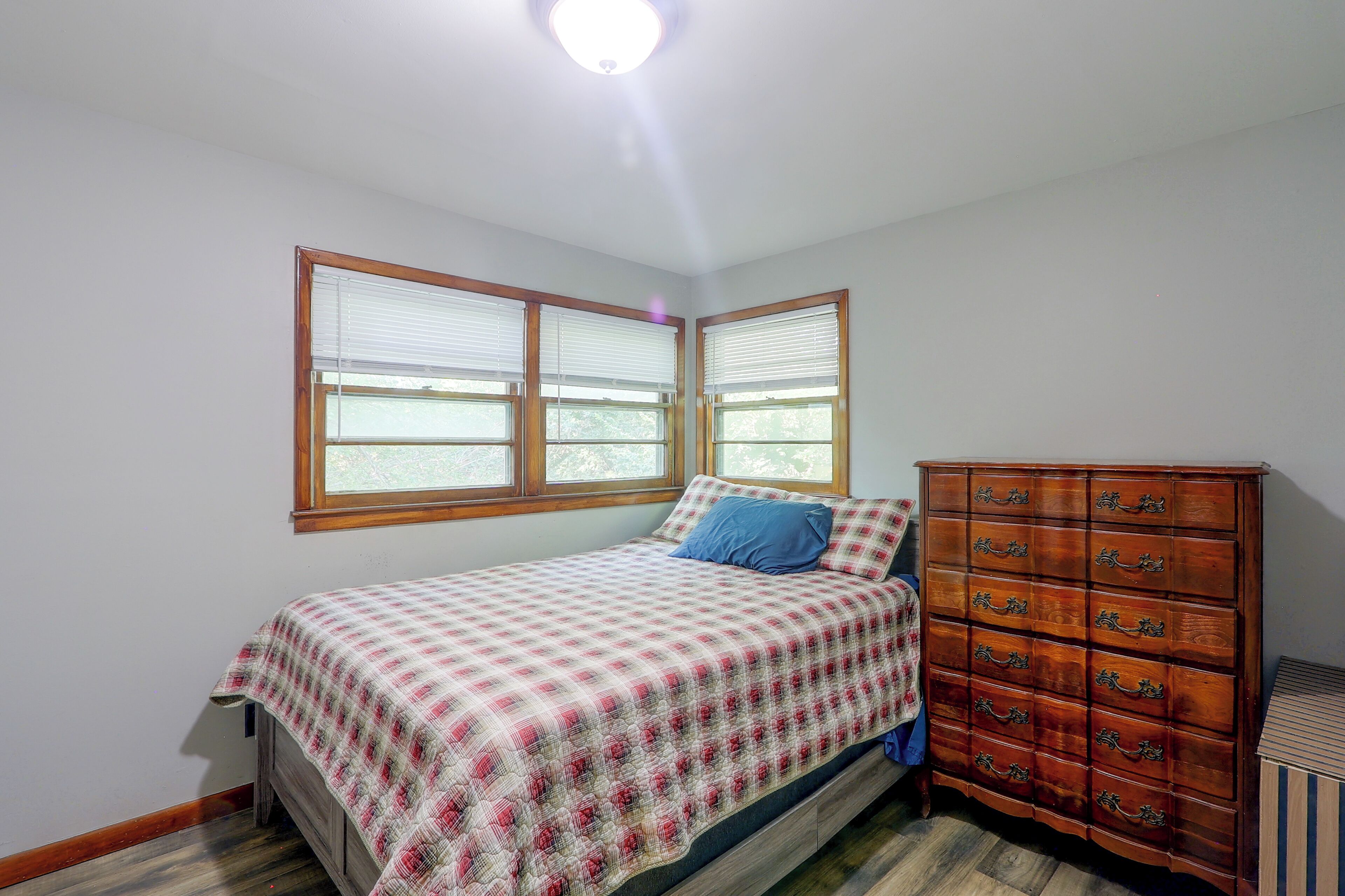 A bedroom with a bed, a dresser, and two windows with blinds.