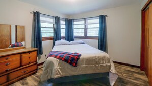 A bedroom with a bed, a dresser, a mirror, and a window with curtains.