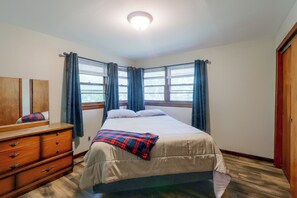 Um quarto com cama, penteadeira, espelho e janela com cortinas.