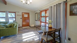A room with a green sofa, wooden dining table, chairs, a wooden door, and a window with curtains.