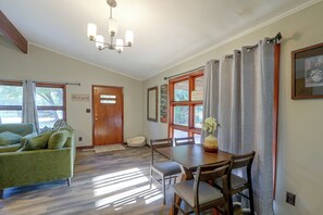 Quarto com sofá verde, mesa de jantar de madeira, cadeiras, porta de madeira e janela com cortinas.