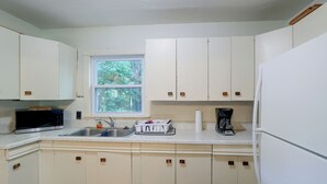 A kitchen with white cabinets, a window, a sink, a microwave, a coffee maker, and a refrigerator.