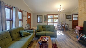 A living room with green sofas, a coffee table, and a dining area with a table and chairs.