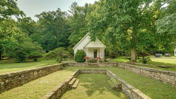 A small white building with a porch, surrounded by a stone wall and grassy area. - Ride, Swim & Hike! Koalin Farms Cottage (Belleview)