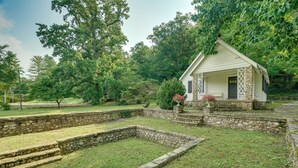 A small stone building with a porch, surrounded by a grassy area and trees. - Ride, Swim & Hike! Koalin Farms Cottage (Belleview)