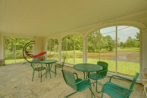 Eine überdachte Terrasse mit einer Hängematte, grünen Metallstühlen und einem Tisch.