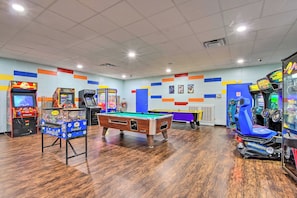 A recreational room with a pool table, arcade games, and a blue racing game machine.