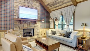 A cozy living room with a stone fireplace, a large flat-screen TV, a sofa, and a coffee table.