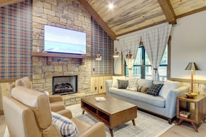 A cozy living room with a stone fireplace, a large flat-screen TV, a sofa, and a coffee table.