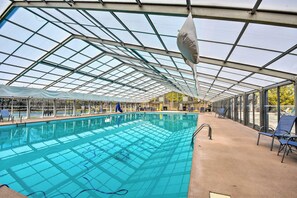 A covered swimming pool with clear glass panels, blue chairs, and a concrete deck.