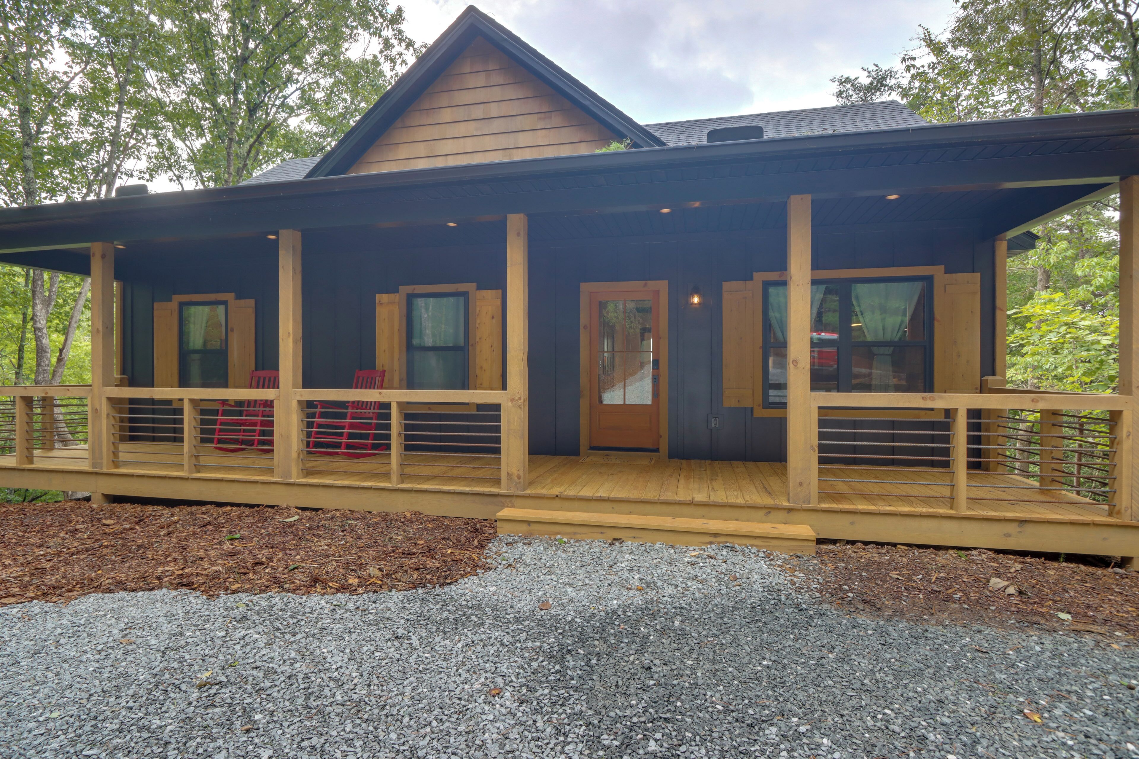 A wooden cabin with a covered porch, multiple windows, and a gravel driveway.