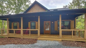A wooden cabin with a covered porch, multiple windows, and a gravel driveway.