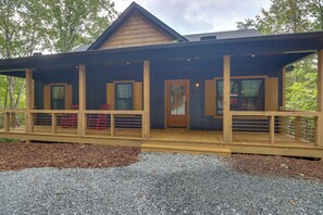 A wooden cabin with a covered porch, multiple windows, and a gravel driveway.