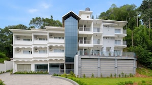 A multi-story hotel with a central glass tower, balconies, and a landscaped garden. - Tripple F Inn - A Luxury Stay in Munnar (Munnar)