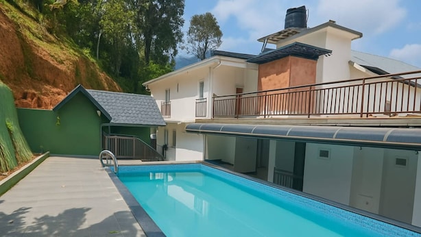 A swimming pool with a tiled deck, a small house-like structure, and a building with a balcony. - Tripple F Inn - A Luxury Stay in Munnar (Munnar)