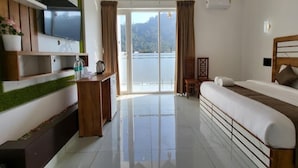 A modern hotel room with a large bed, a TV mounted on the wall, a desk with a kettle, and a view of a body of water through the sliding doors. - Tripple F Inn - A Luxury Stay in Munnar (Munnar)