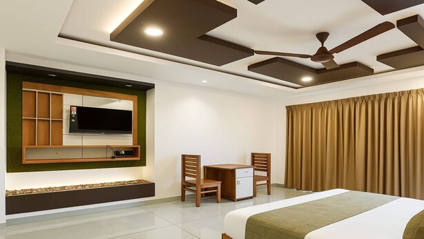 A hotel room with a bed, a desk, two chairs, a television, and a ceiling fan. - Tripple F Inn - A Luxury Stay in Munnar (Munnar)