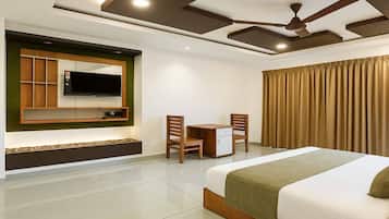 A hotel room with a bed, a desk, two chairs, a television, and a ceiling fan.