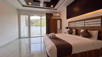 A modern hotel room with a large bed, a ceiling fan, and a view of a body of water through the sliding glass door.