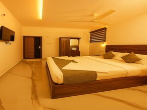 A hotel room with a bed, a ceiling fan, a TV mounted on the wall, and a wooden wardrobe. - Tripple F Inn - A Luxury Stay in Munnar (Devikolam)