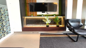 A modern waiting area with a flat-screen TV mounted on a wall, a seating area with a black leather chair, and a decorative plant arrangement. - Tripple F Inn - A Luxury Stay in Munnar (Munnar)