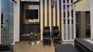 A modern living room with a flat-screen TV, two black chairs, a potted plant, and a sliding glass door leading to a balcony. - Tripple F Inn - A Luxury Stay in Munnar (Munnar)